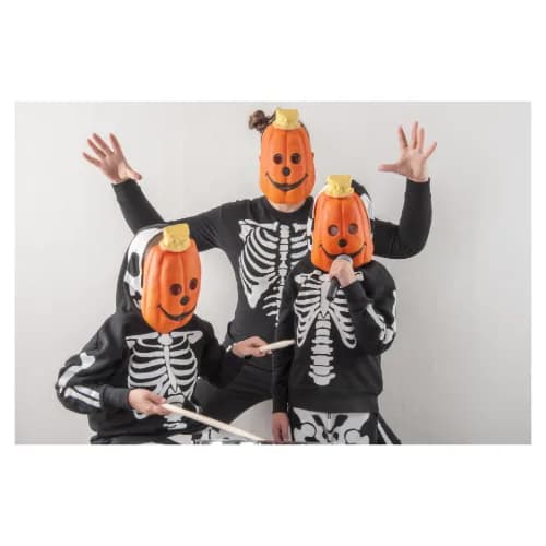 Three children dressed as pumpkins holding drumsticks and a microphone.