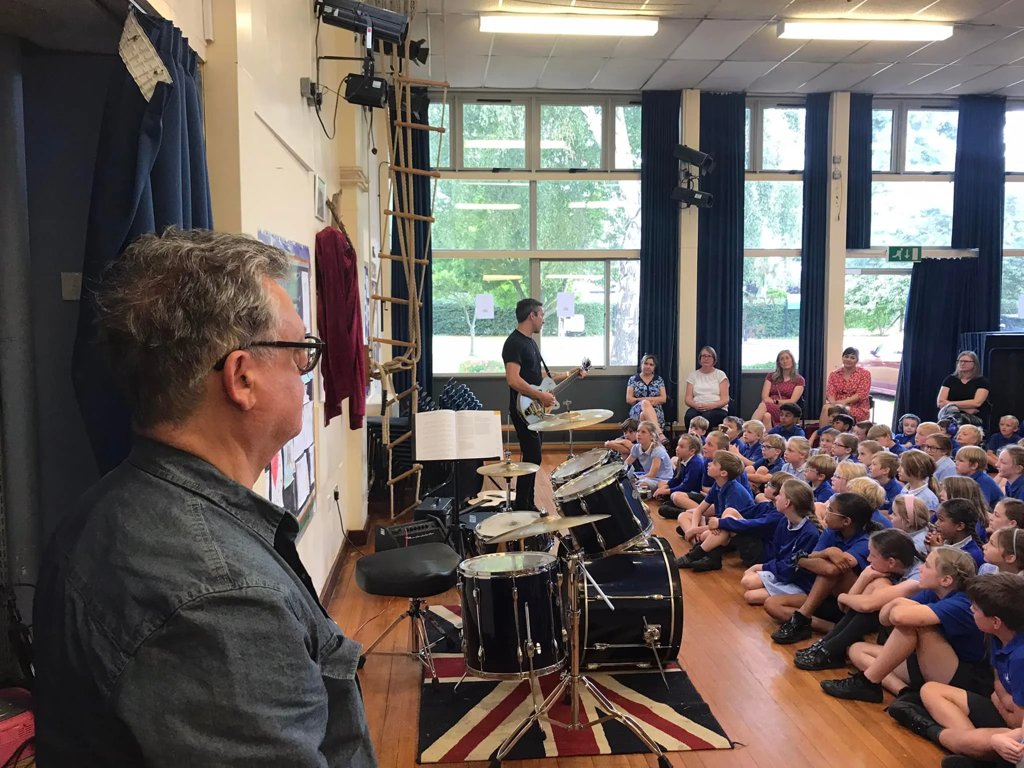 Guitar tutor performing in front of a school assembly, engaging with the audience.
