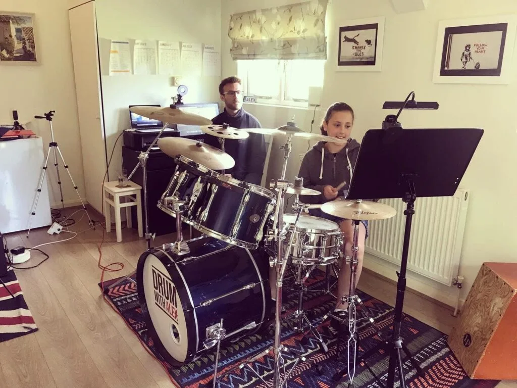 Drum student practicing on a drum kit with tutor guiding her
